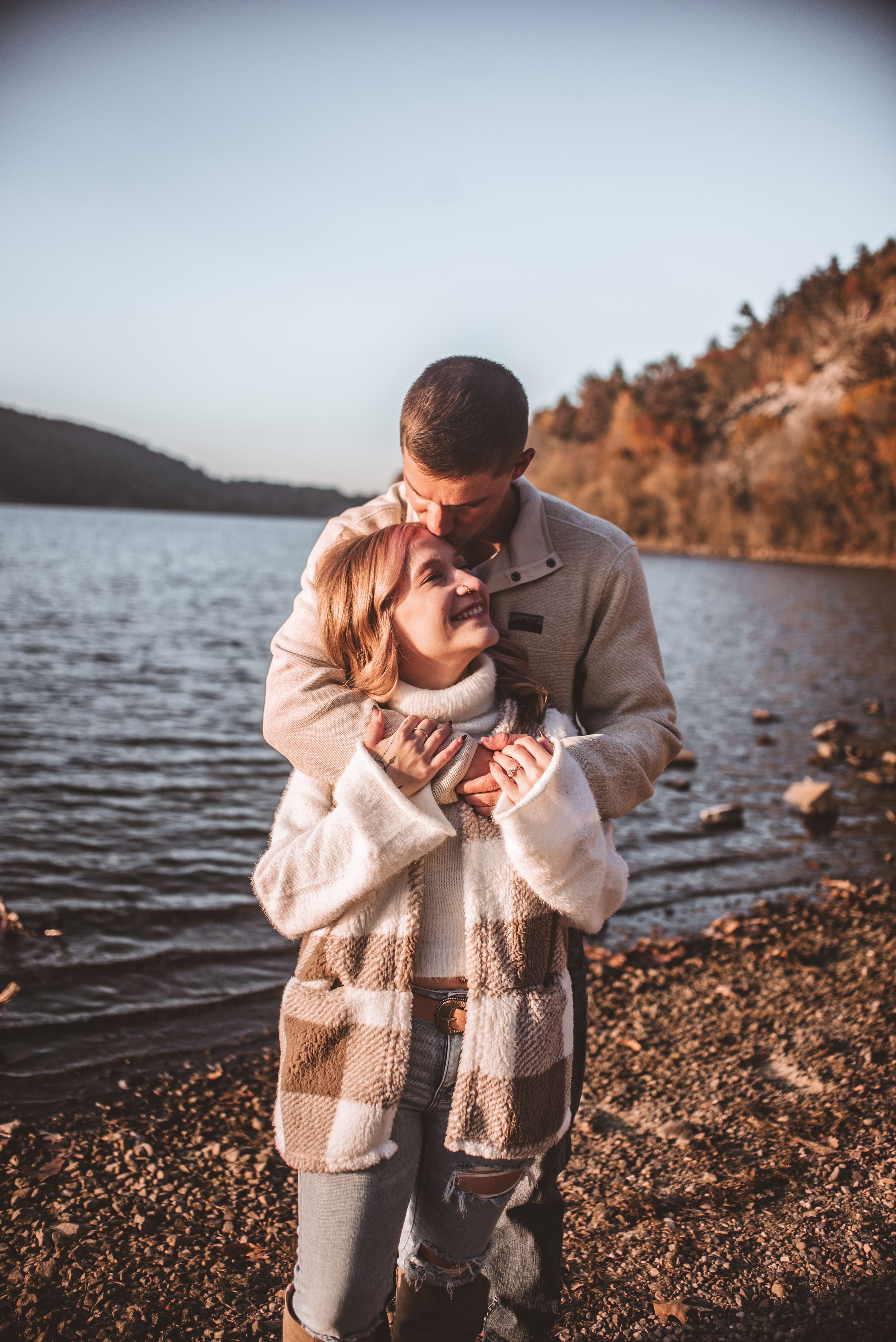 Intimate moment shared on lakeside beach during golden hour.