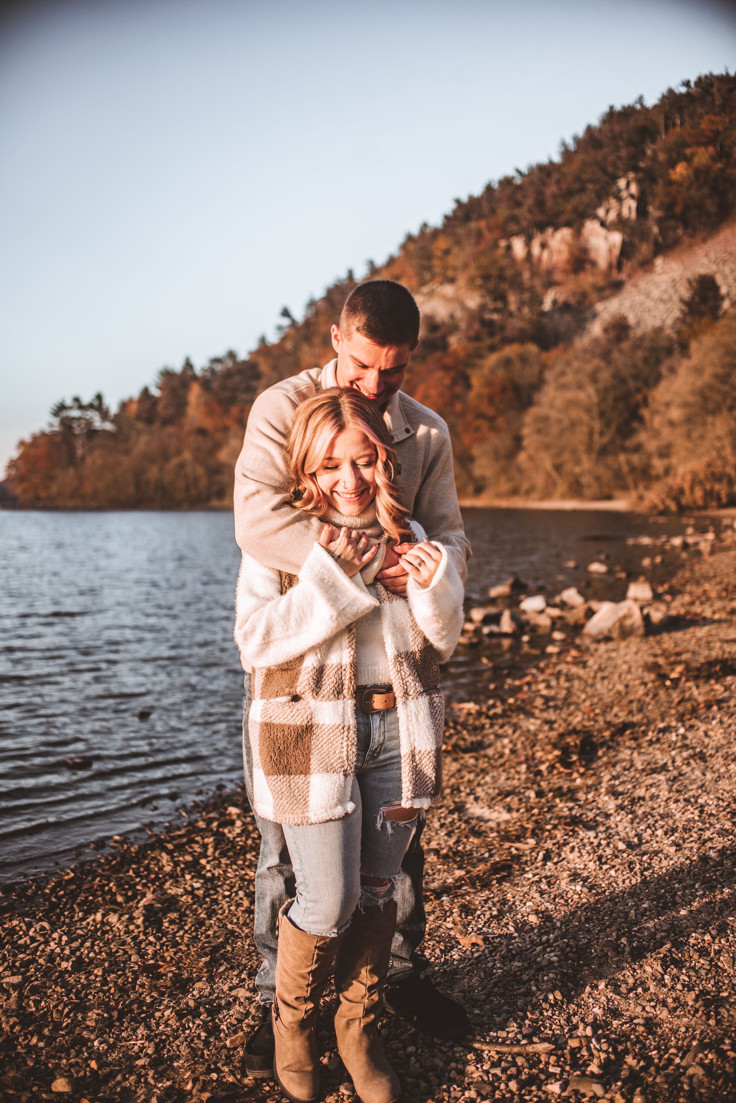 A romantic autumn photoshoot by a lakeside beach with warm sunset lighting and cozy sweaters.