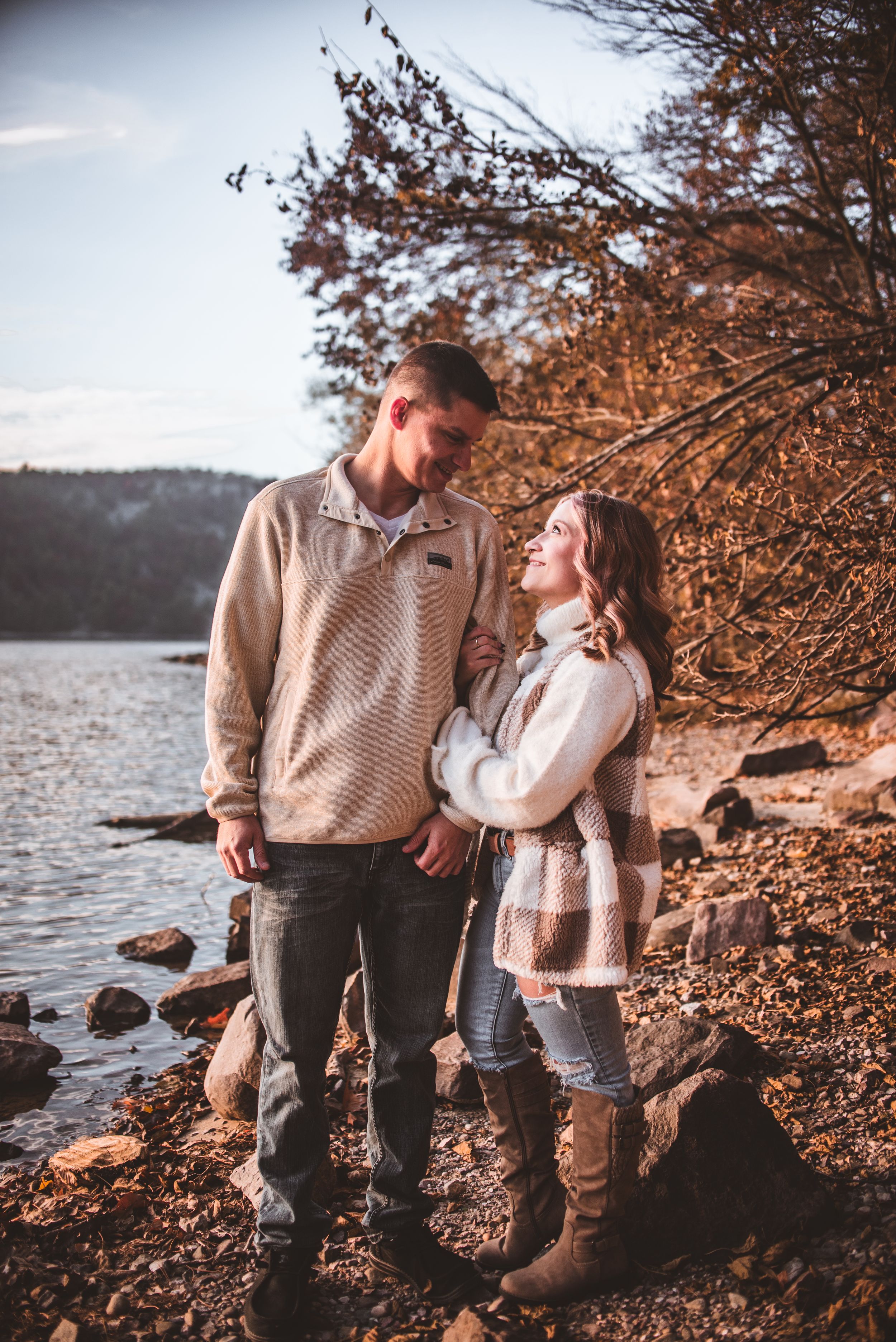 A scenic fall engagement photo with colorful autumn foliage along a rocky lakeshore.
