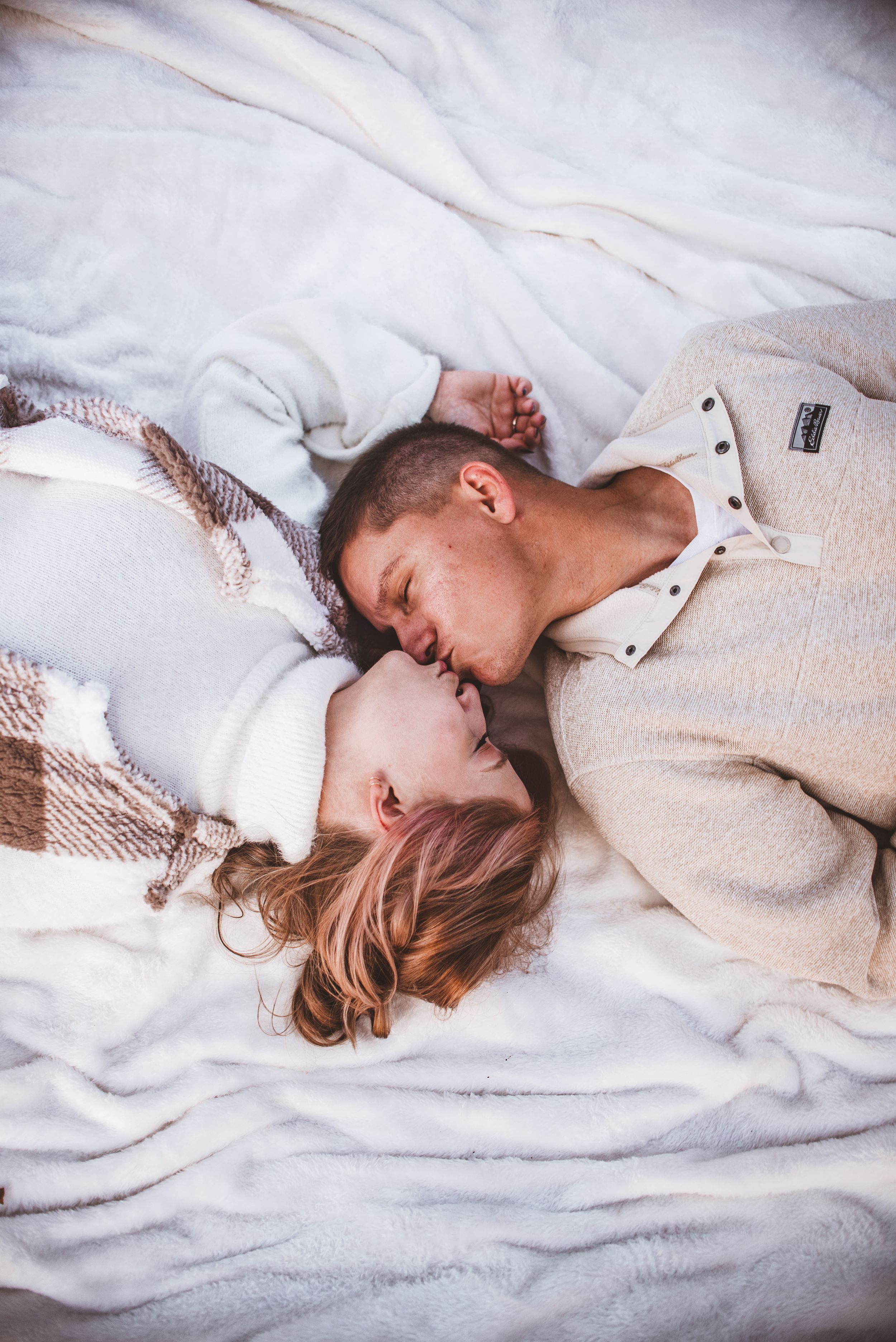 An intimate portrait on white bedding with soft natural lighting and matching beige sweaters.