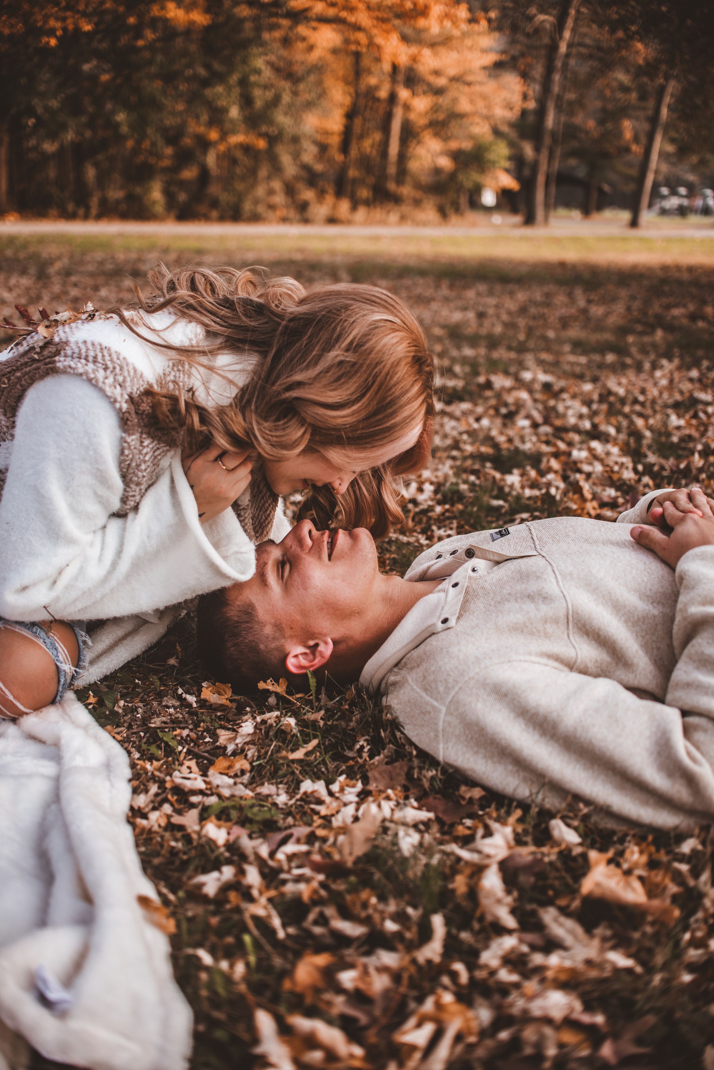 A playful autumn photoshoot among fallen leaves with warm evening light filtering through trees.