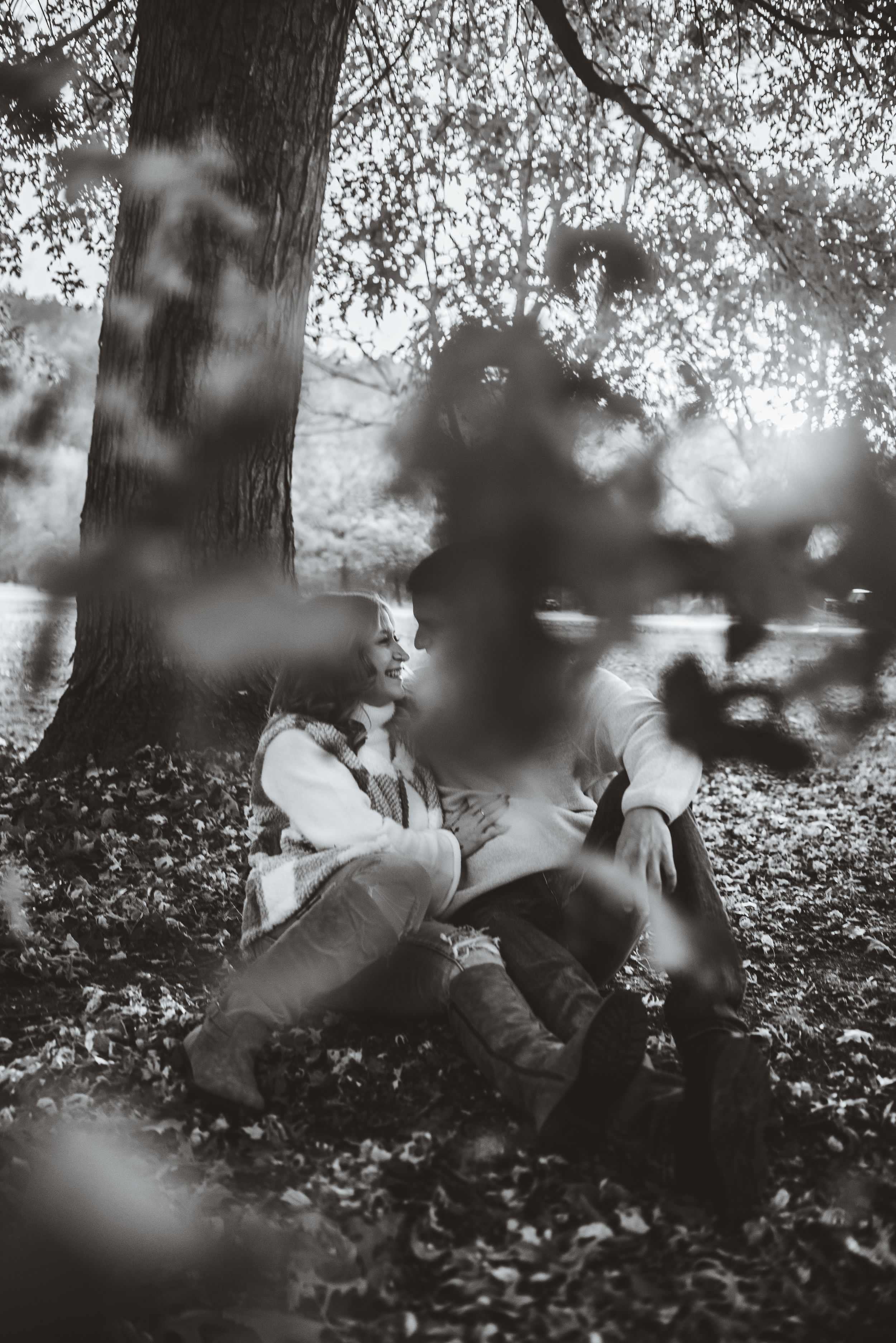 An artistic black and white portrait through blurred foreground elements in a fall setting.
