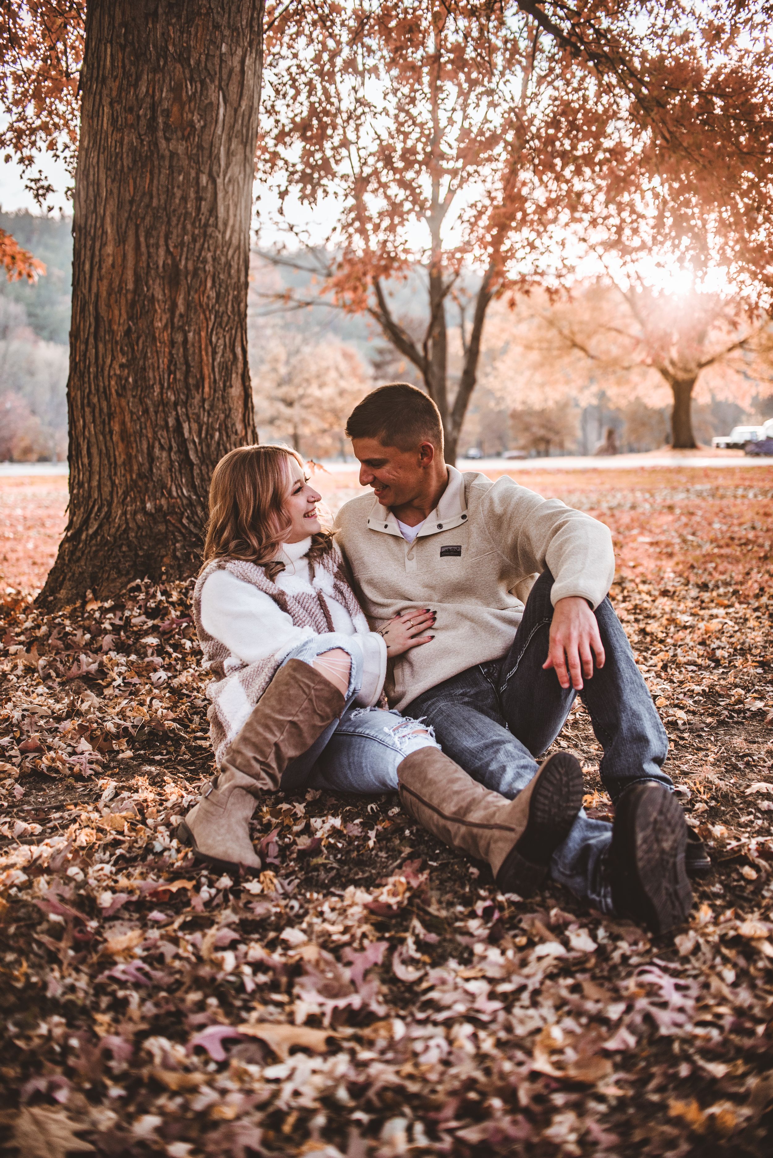 A candid autumn portrait under a large tree with golden sunlight filtering through falling leaves.