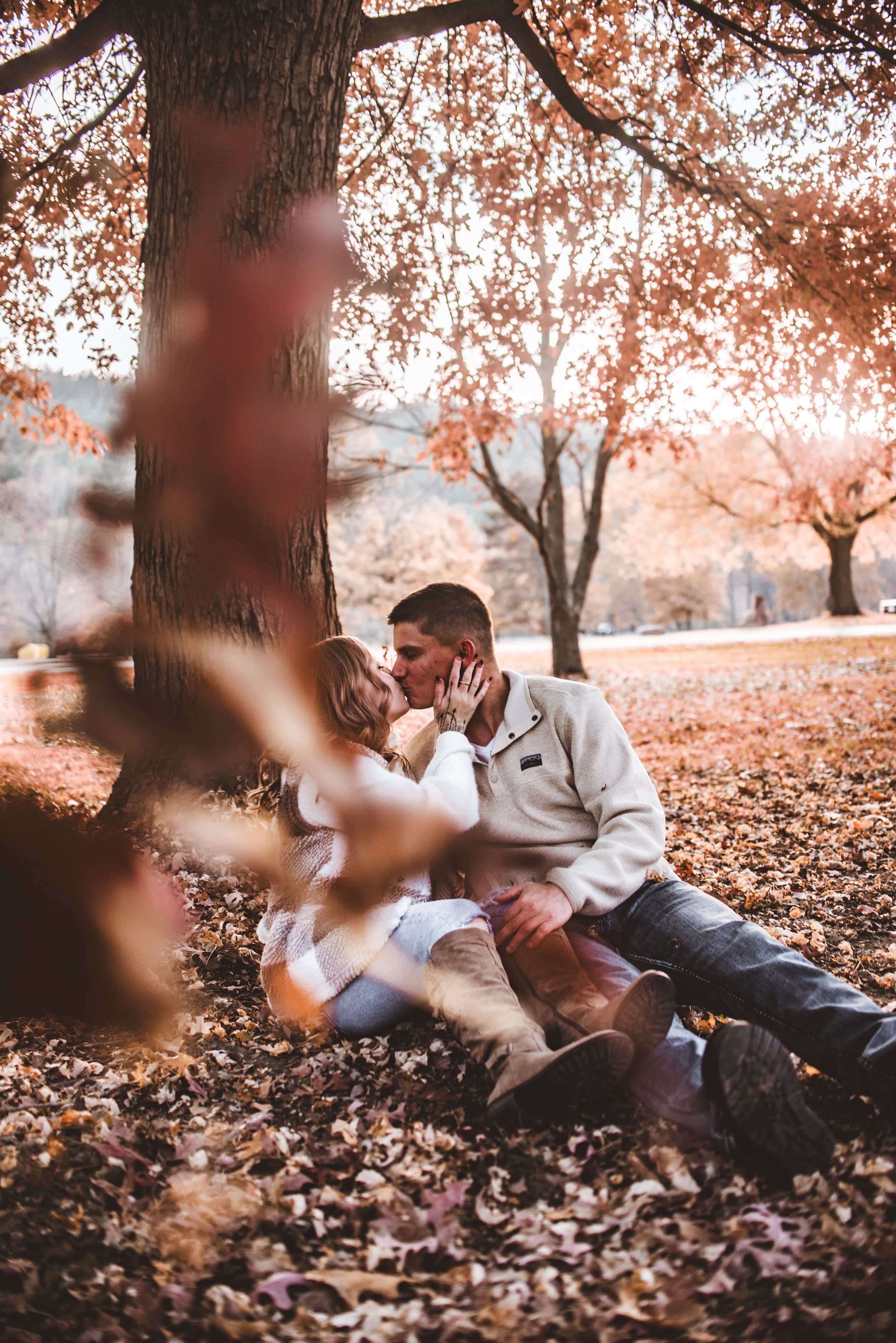 An intimate fall portrait beneath a tree with warm sunset tones and scattered autumn leaves.