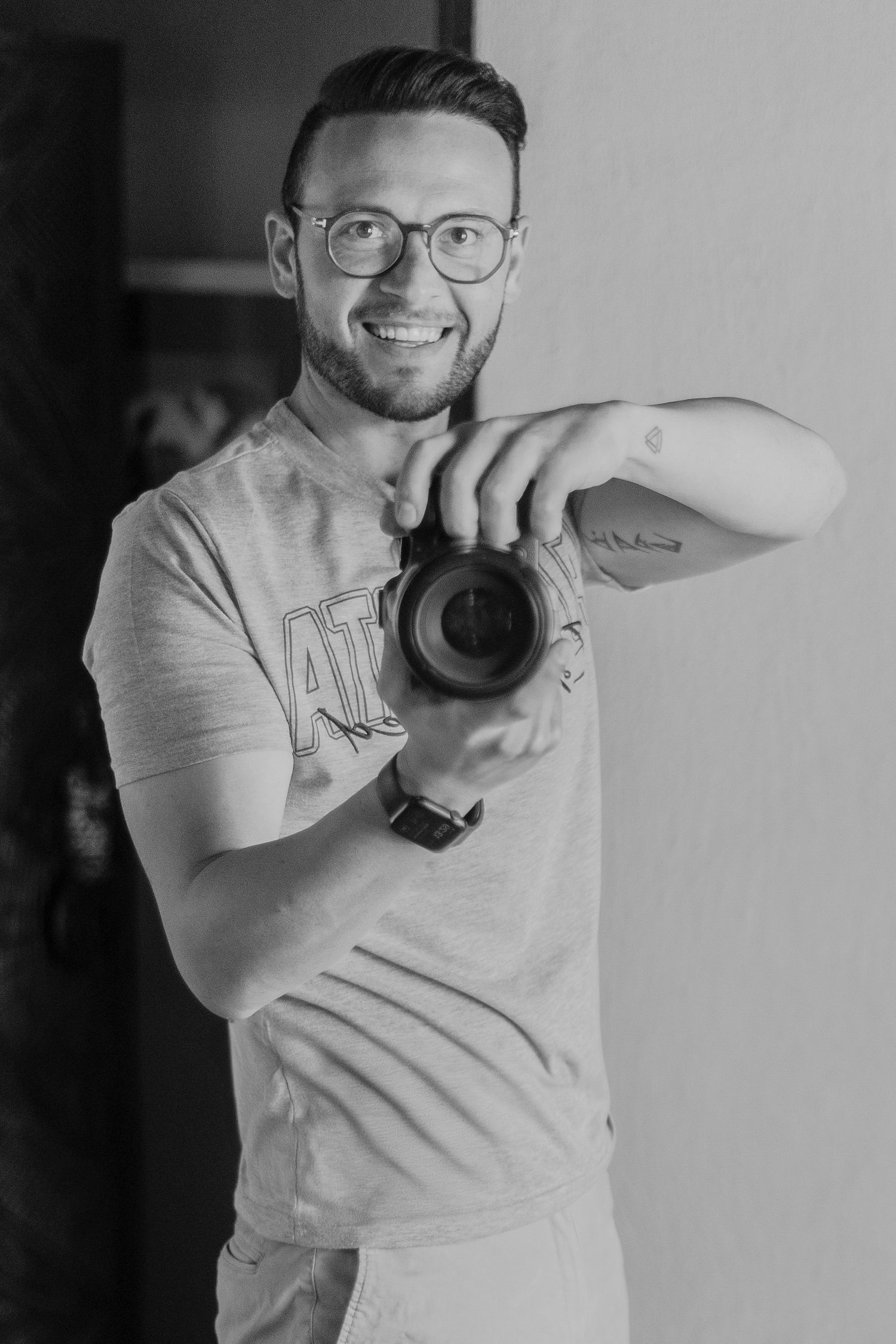 Smiling male photographer holding camera lens in black and white portrait photo.