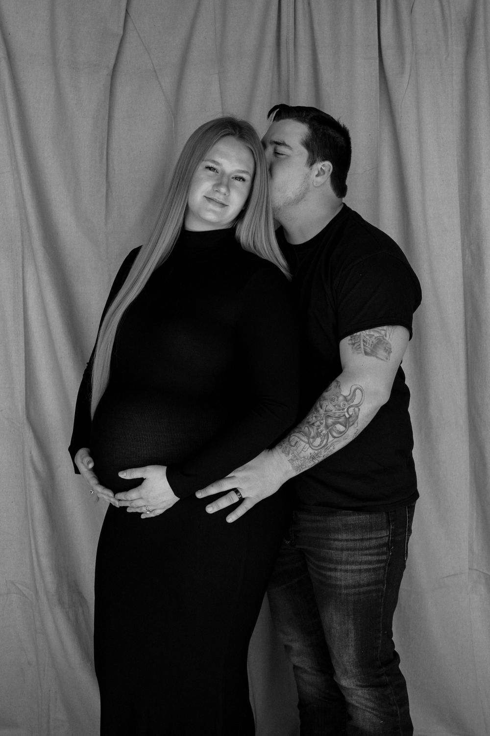 Black and white maternity portrait of an expecting couple embracing and smiling together.