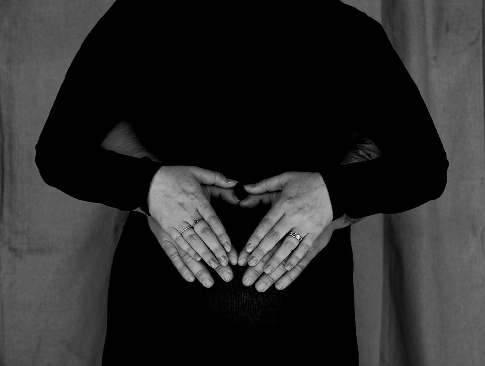 Black and white maternity portrait featuring hands forming a heart shape over a pregnant belly.