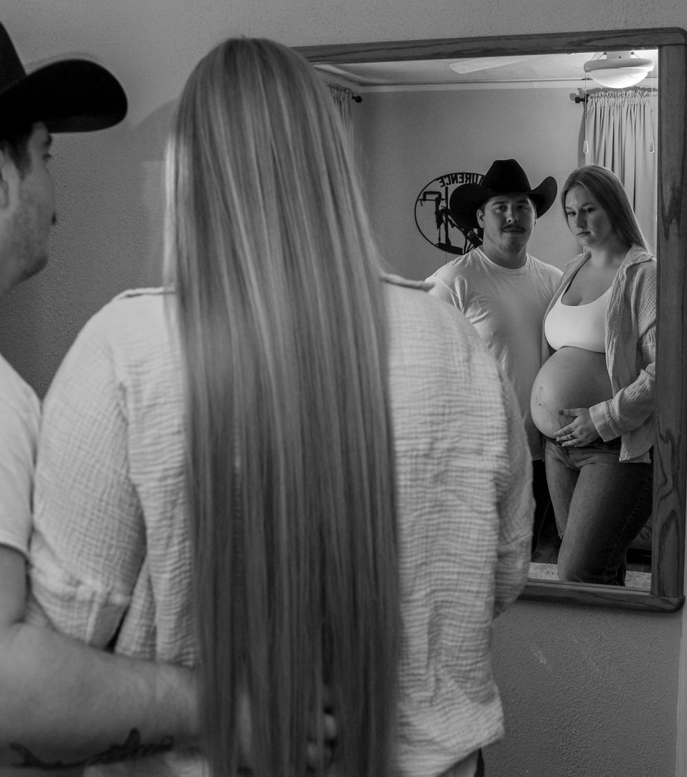 Black and white maternity photo capturing an expecting mother reflected in a mirror during a special moment.