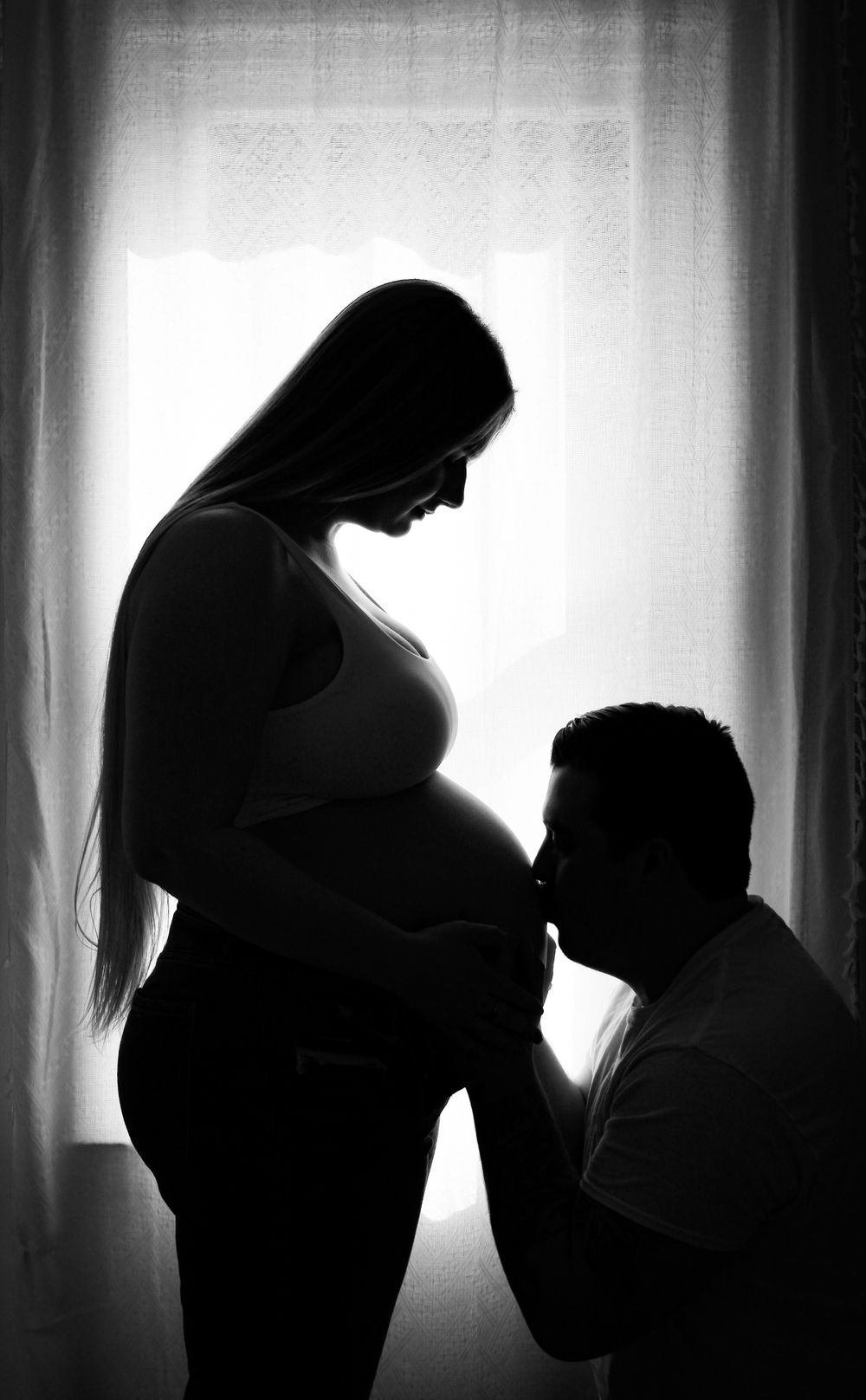 Silhouette maternity portrait of an expecting couple sharing a special moment beside a window.