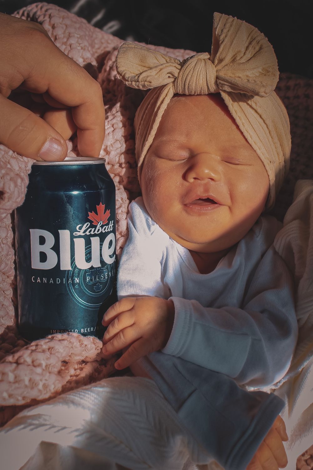 Sleeping newborn baby wearing a bow headband beside a beverage can during a lifestyle newborn session.