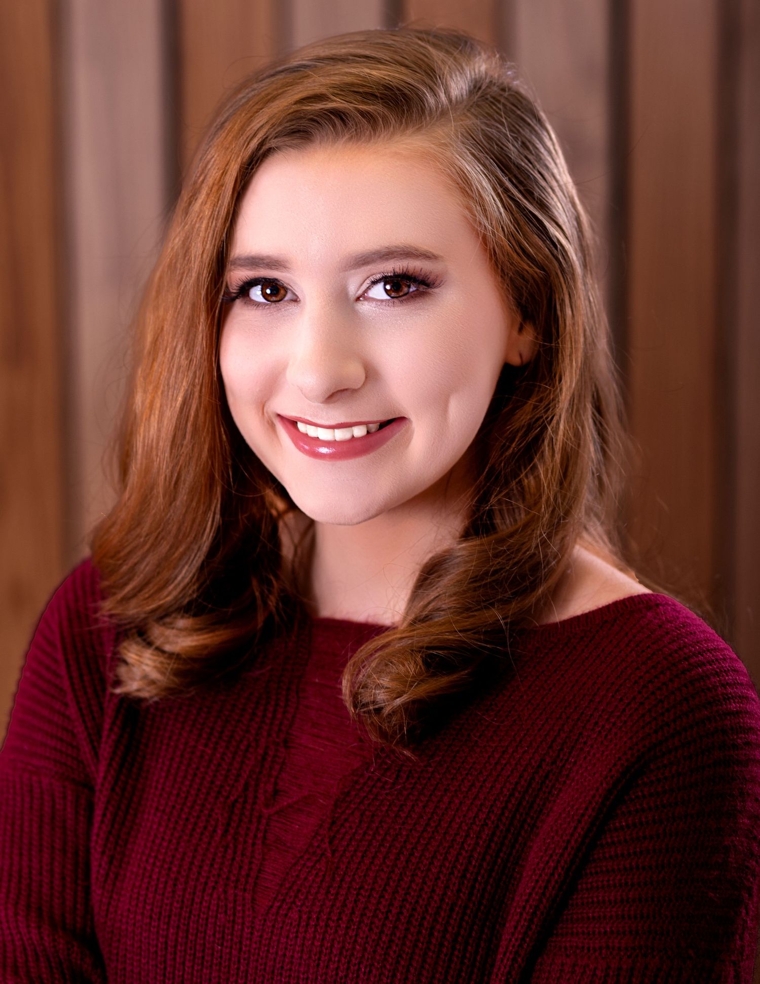 Portrait of woman in burgundy sweater against wood panel background.