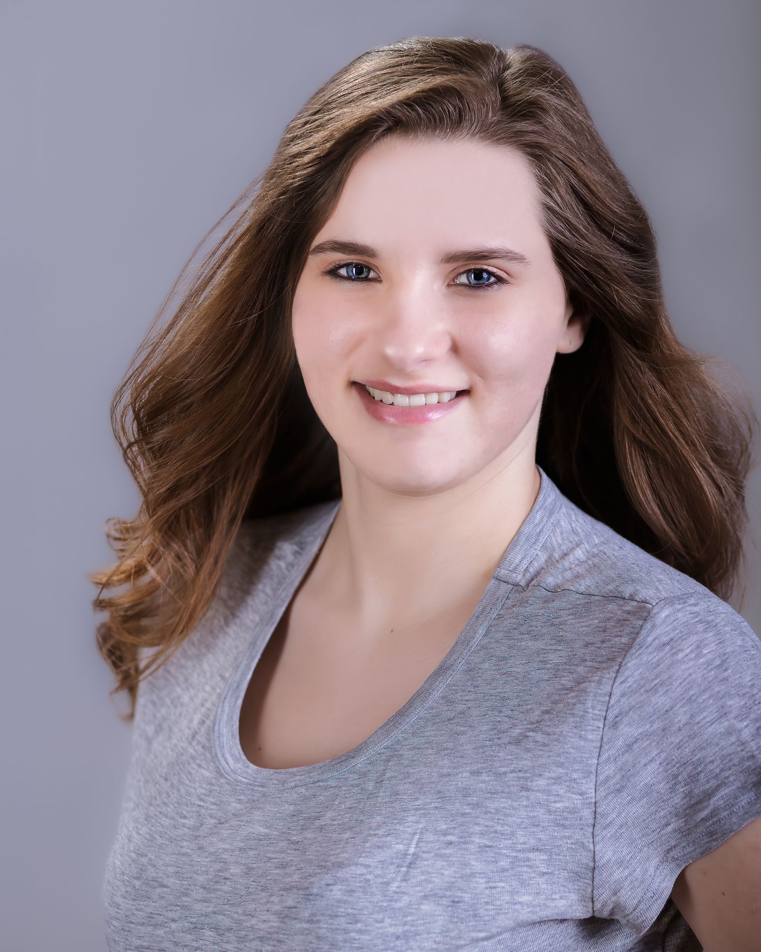 Portrait of someone in a gray top with wavy brown hair and warm smile.