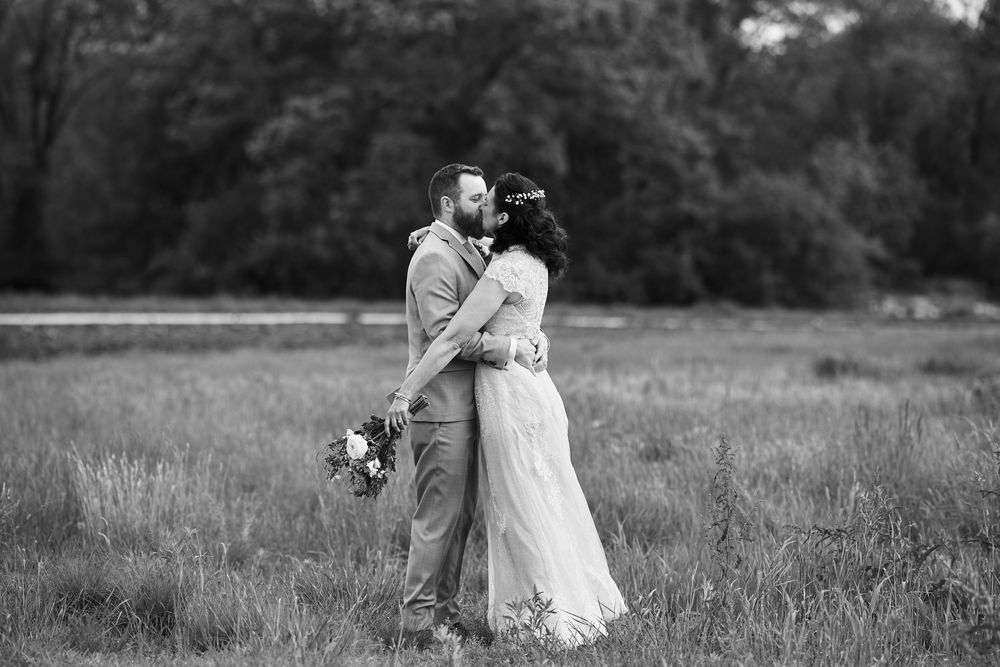 A romantic couple embraces in a serene meadow field during a black and white outdoor photoshoot.