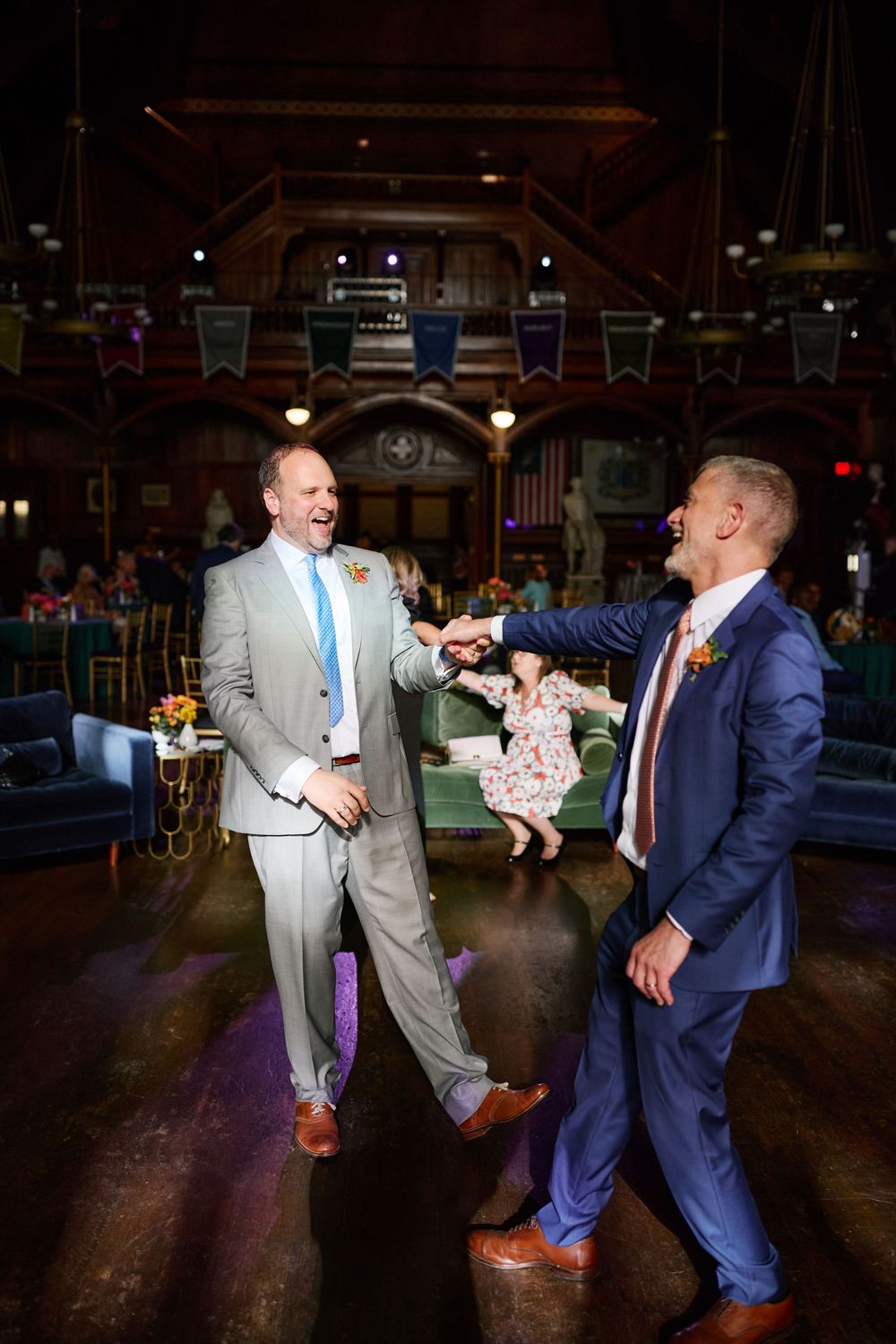 Two people in formal attire dance playfully on a dark dance floor during a celebration event.