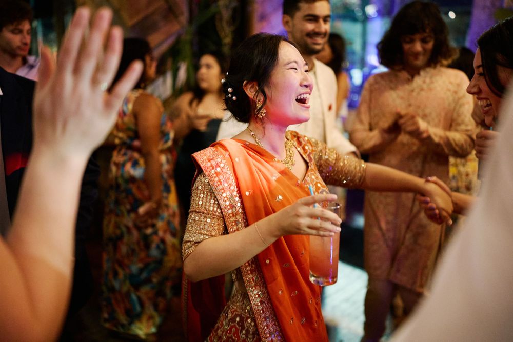 People dancing and celebrating at a festive Indian wedding reception with colorful traditional attire and raised hands.