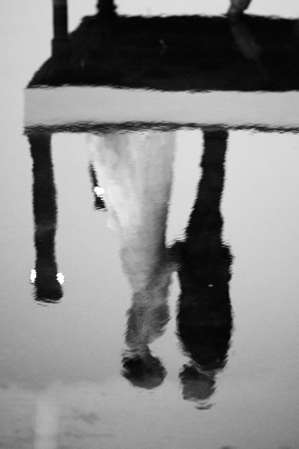 Black and white artistic photograph showing legs and feet dangling from above, creating a striking reflection effect.