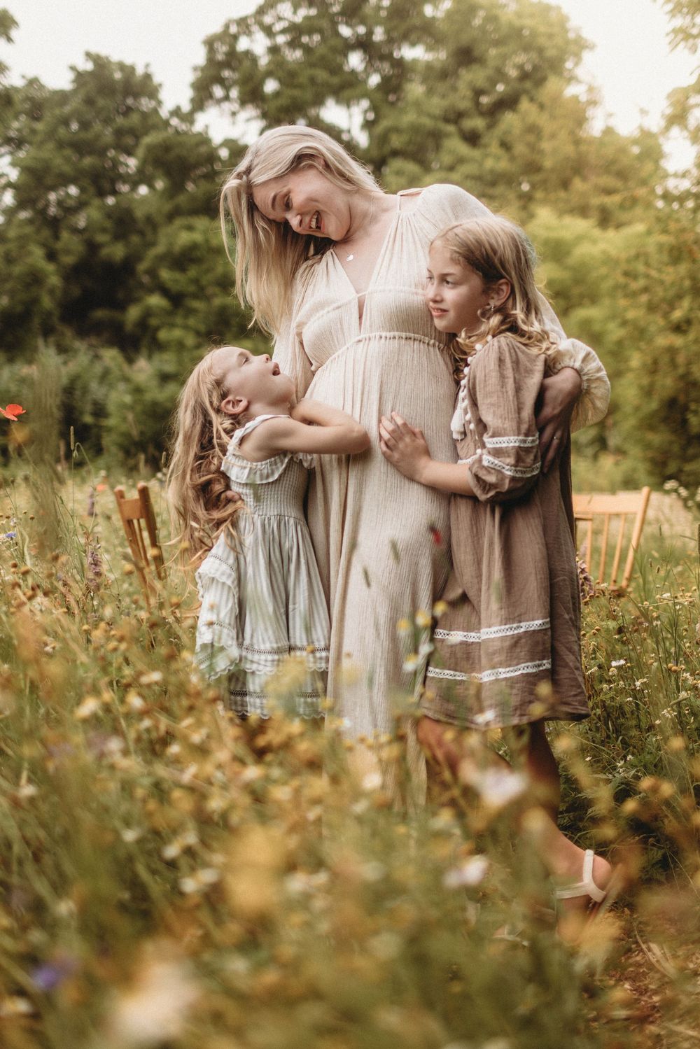 Family wearing vintage-style dresses standing together in a wildflower meadow at sunset.