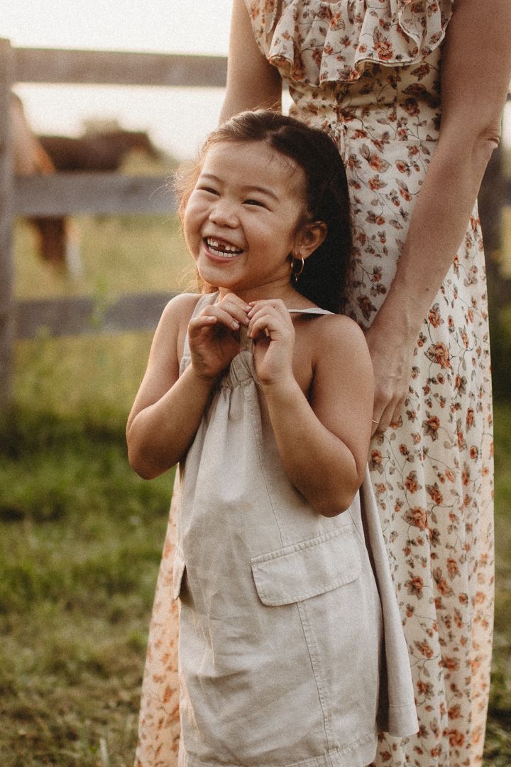 Child in beige dress laughing joyfully in outdoor setting.