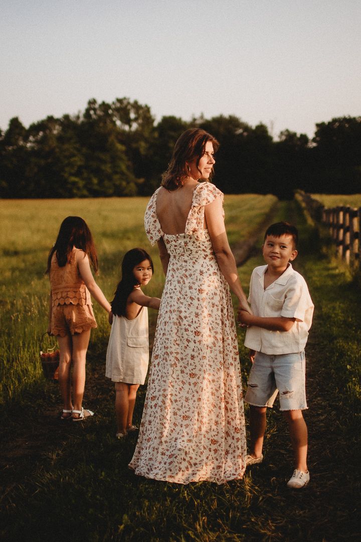 Family enjoying sunset together in grassy field wearing floral dresses.