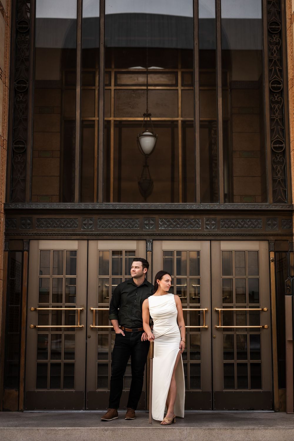 Elegant couple posing before building doors, woman in white gown, man in black attire. Albuquerque New Mexico Engagement photographer