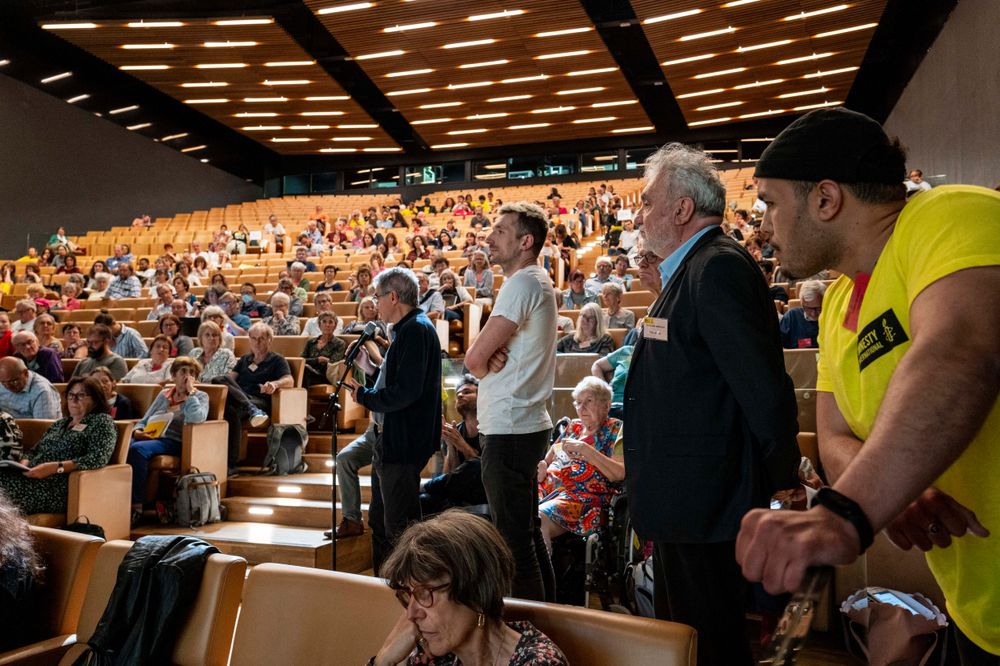 Crowded auditorium filled with spectators during an indoor event with distinctive ceiling lighting.