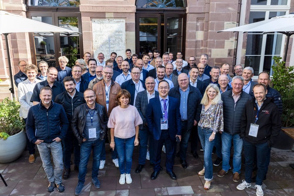 A group of conference attendees gather together for group photos outside a building.