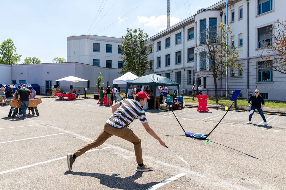 Students play sports and games on an outdoor court at a school with white buildings in the background during daytime.
