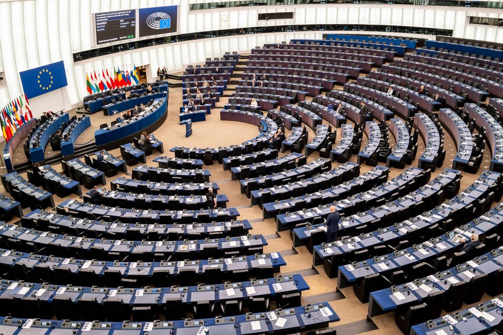 View of the curved semicircle chamber of the European Parliament with its blue seats arranged in a tiered amphitheater layout.