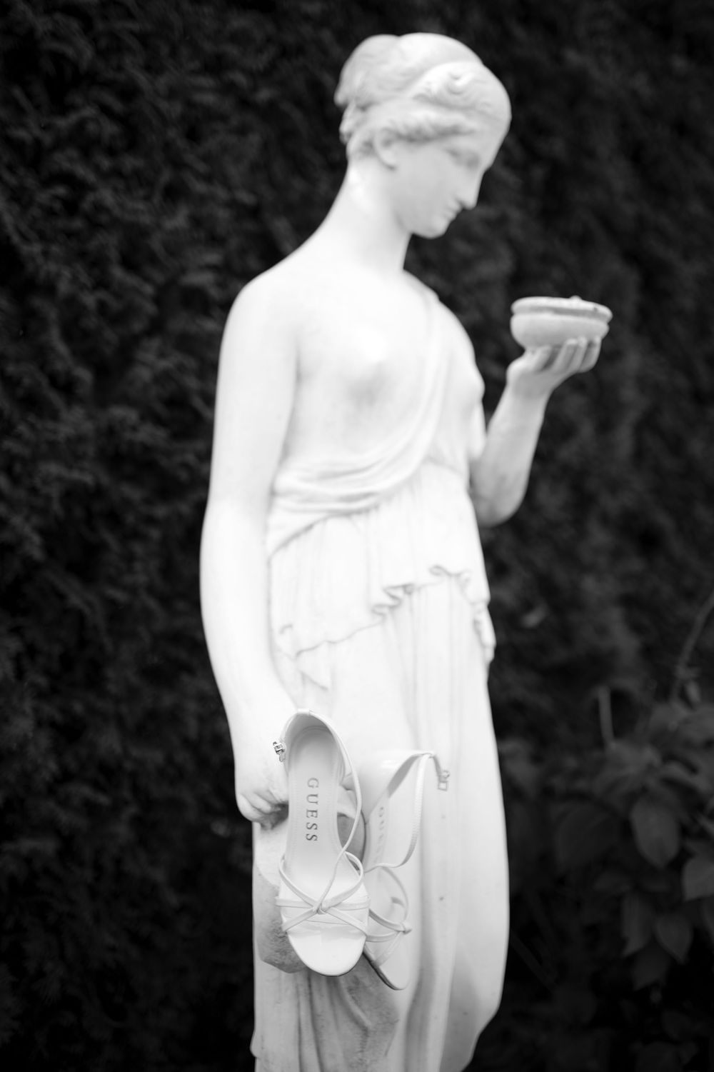 Classic white marble statue holding a bowl while gracefully holding ballet slippers against flowing robes.