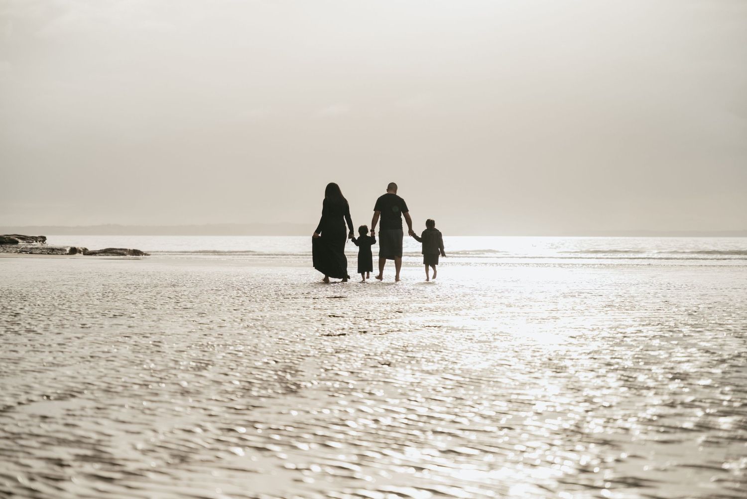 Three silhouettes walking together on a wide sandy beach at sunset.