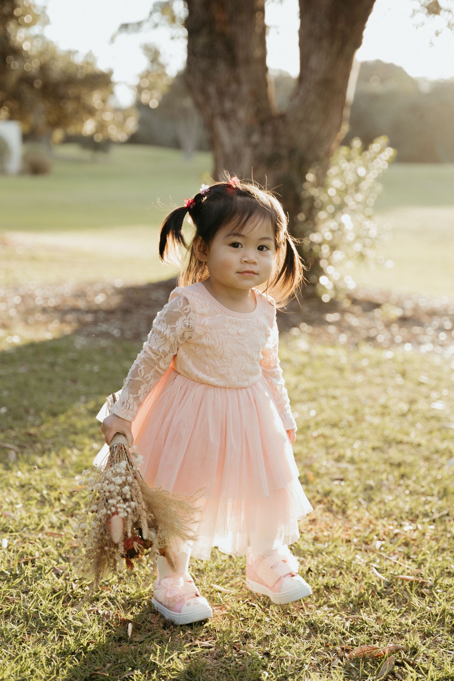 A young child in a pink lacy dress poses outdoors during golden hour.