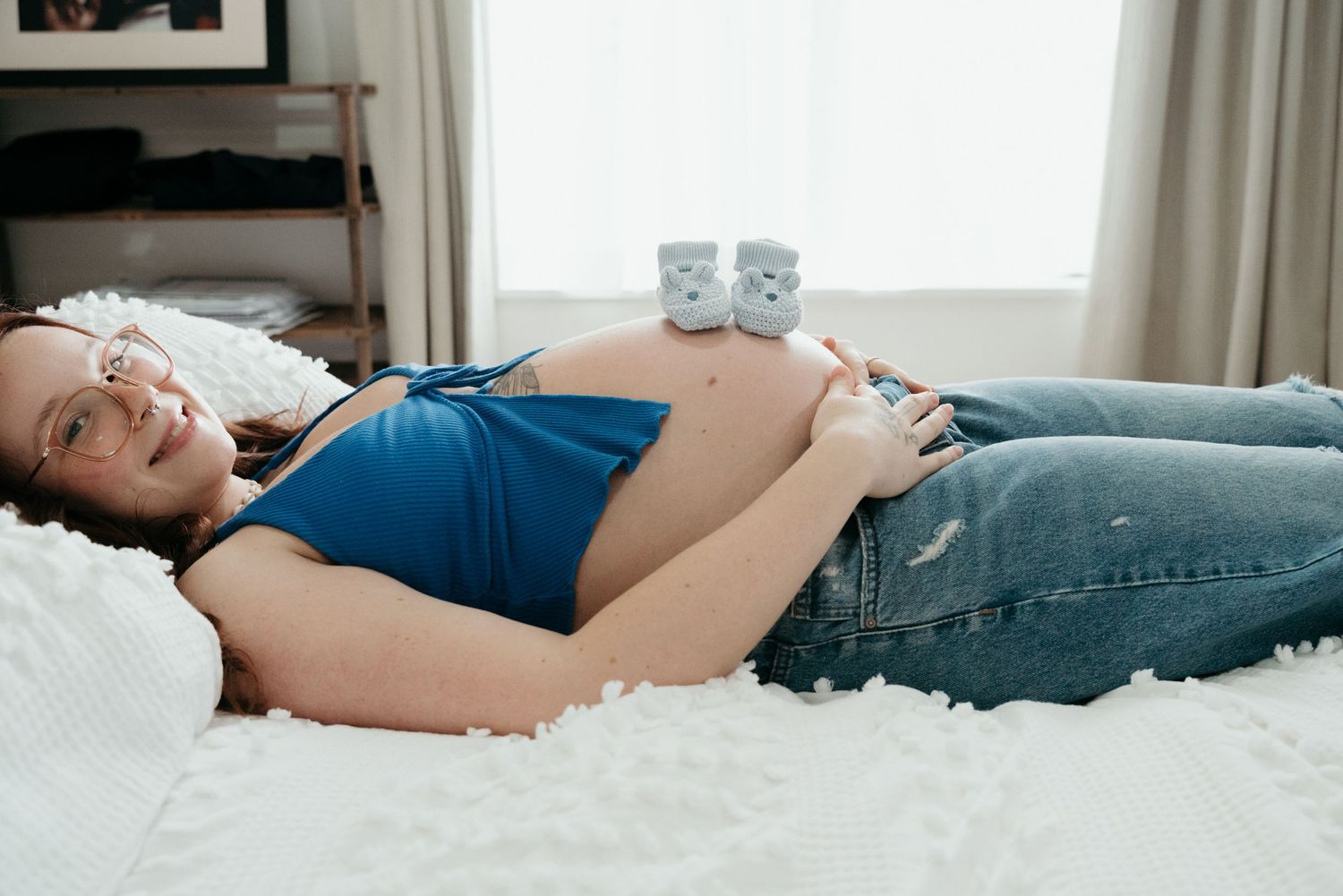 Expecting mother relaxing on white bedding with coffee mugs in the background.