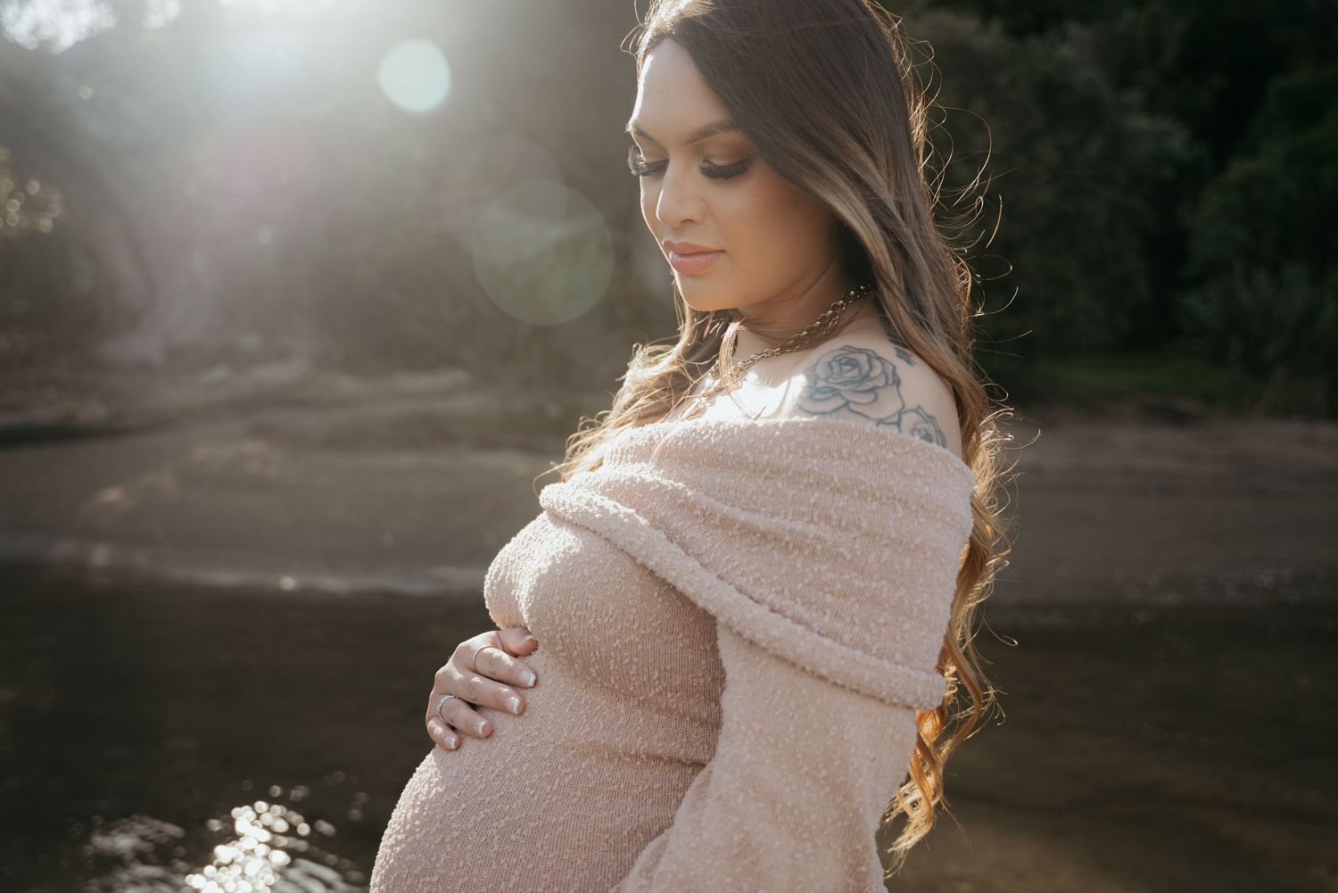 Maternity photo of woman in pink sweater during golden hour.