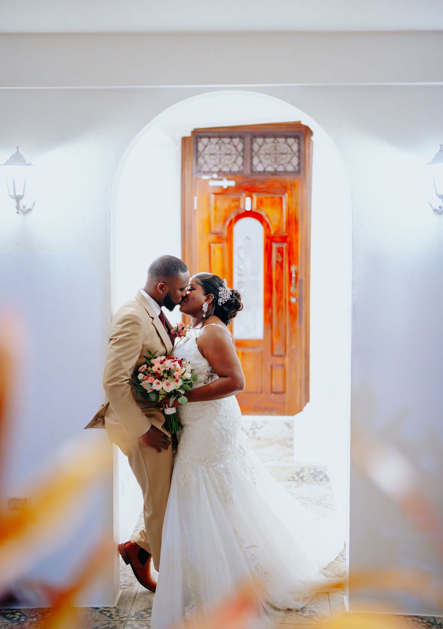 Romantic wedding portrait in white archway with ornate orange door.