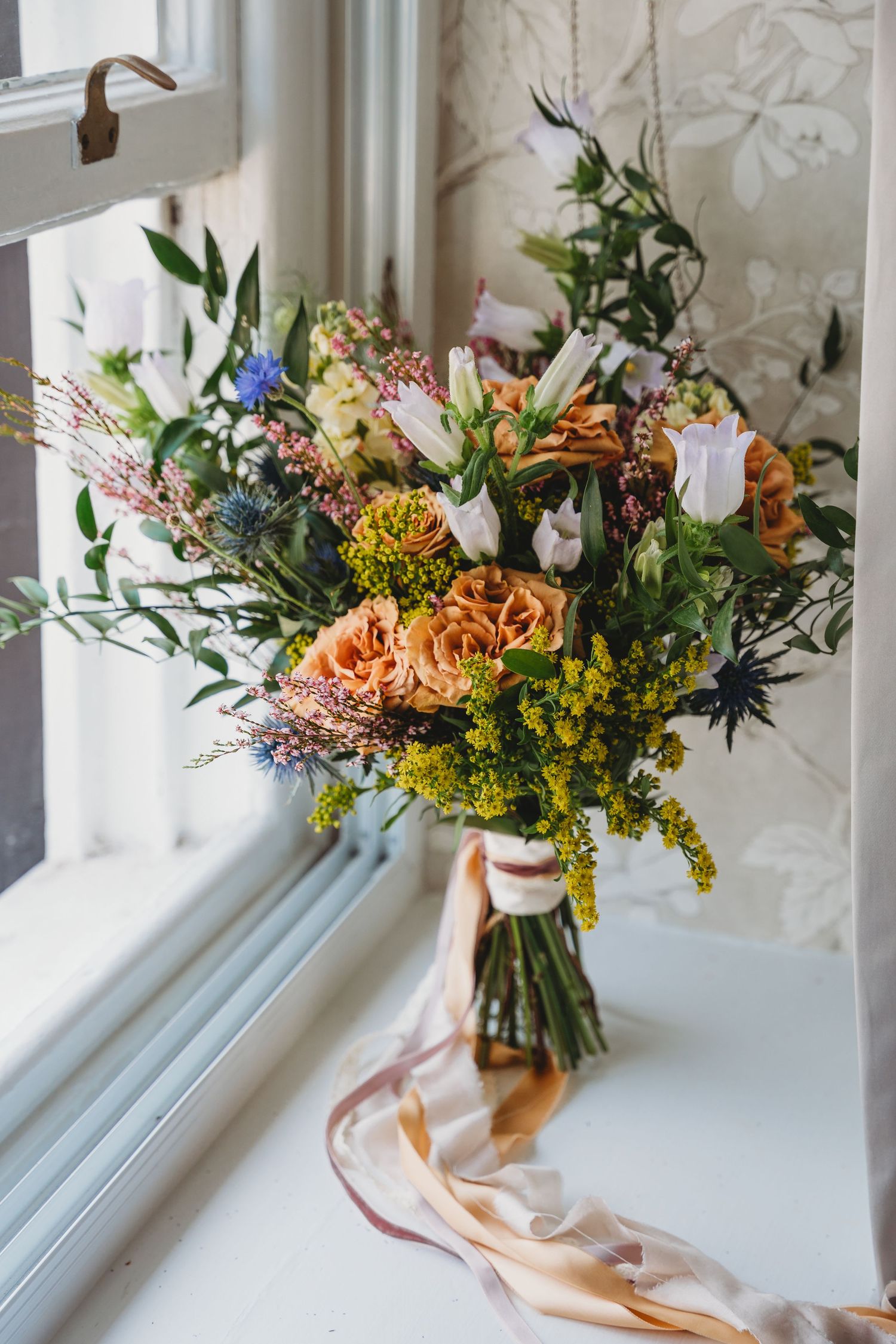 Elegant floral arrangement with orange and yellow blooms in vase by bright window.