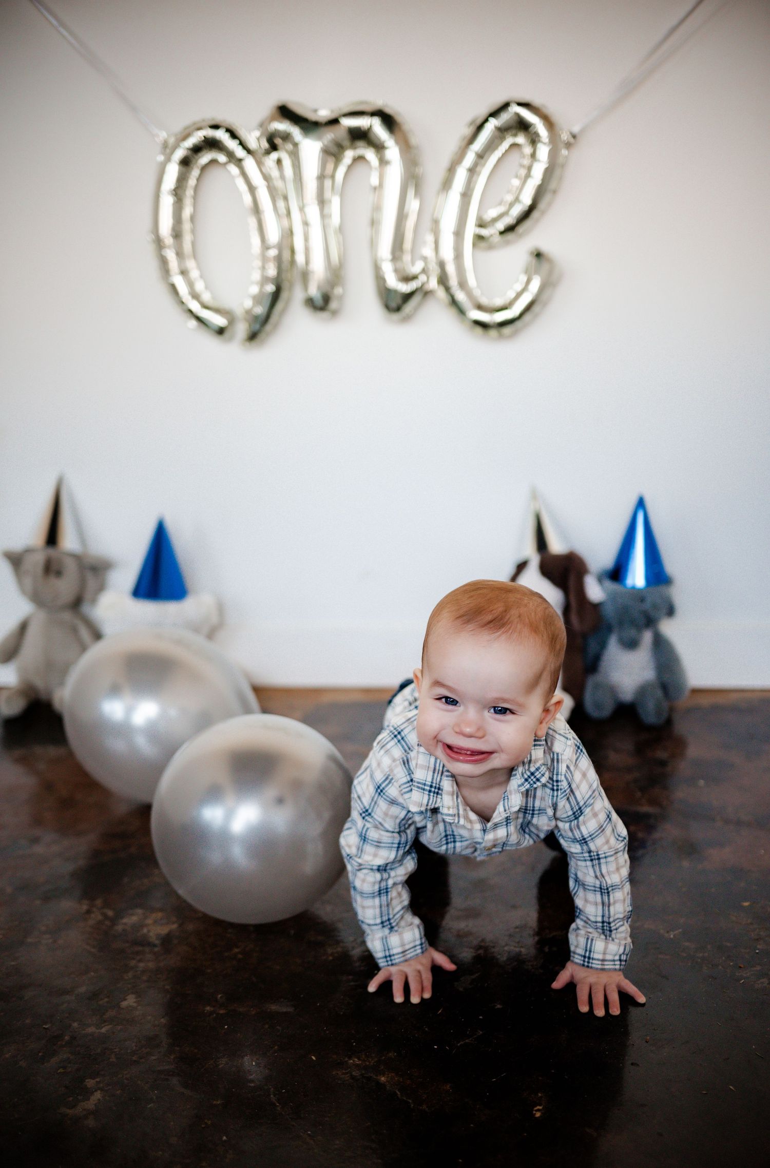 Baby crawling on dark floor with silver balloons and party decorations in background.
