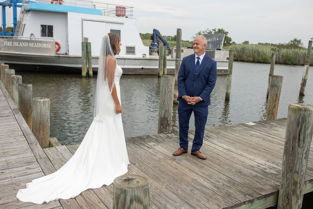 Emotional first look moment between bride in white gown and groom in navy suit on waterfront dock.
