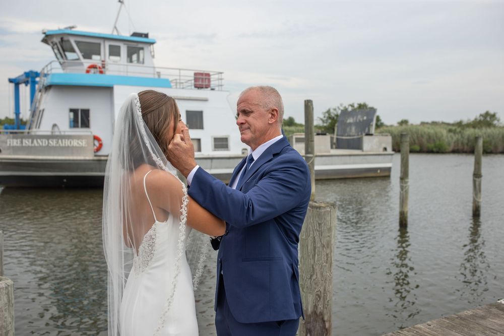 Father adjusts his daughters veil on a waterfront dock before her wedding ceremony.
