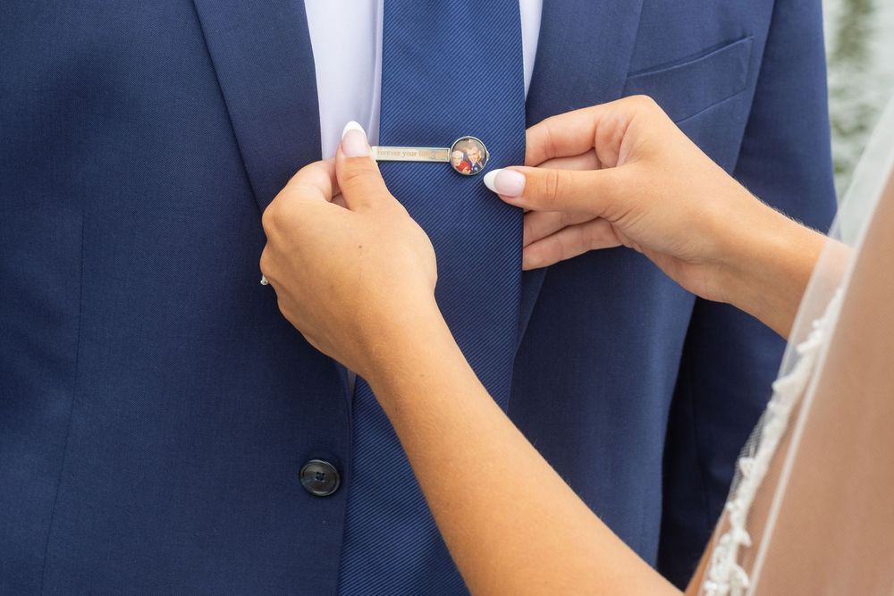 Close-up of hands pinning a boutonniere onto a navy blue suit jacket at a wedding.