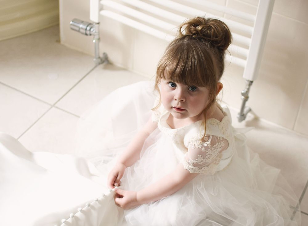 Daughter of the bride playing with the bottom of her mothers dress, looking up into the camera at Balgeddie House Hotel.