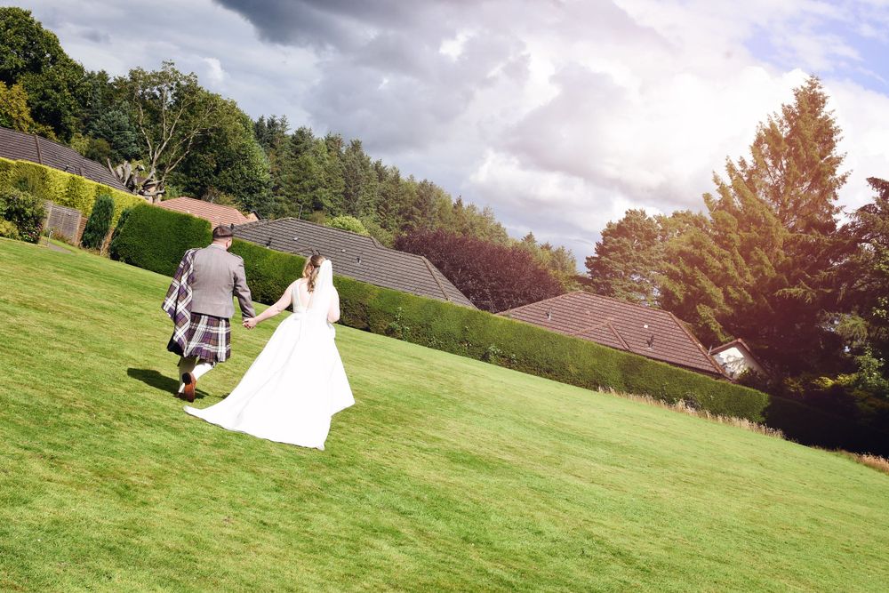 Bride and Groom walk hand and hand, relaxed and content through the Balgeddie House Hotel Gardens after their wedding reception.