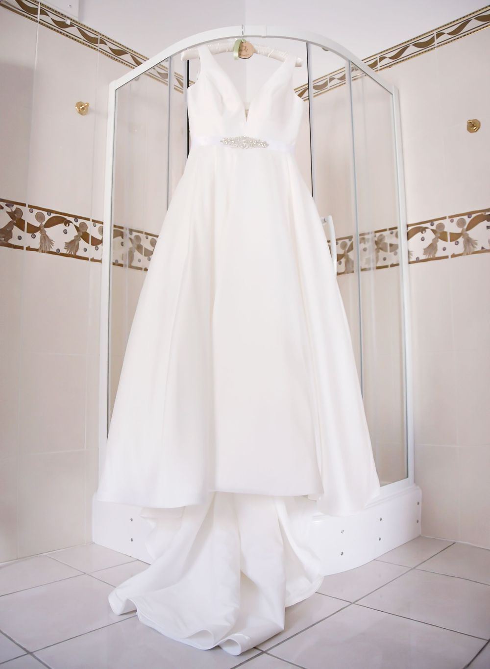 Image of a wedding dress hanging in a bathroom. Elegantly place to show the beautiful detail and waiting for the bride to put it on.