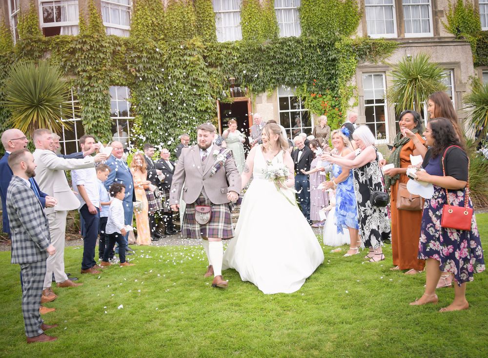 Bride and Groom walk through their guests after their wedding ceremony, their guests throw confetti at Balgeddie House Hotel.