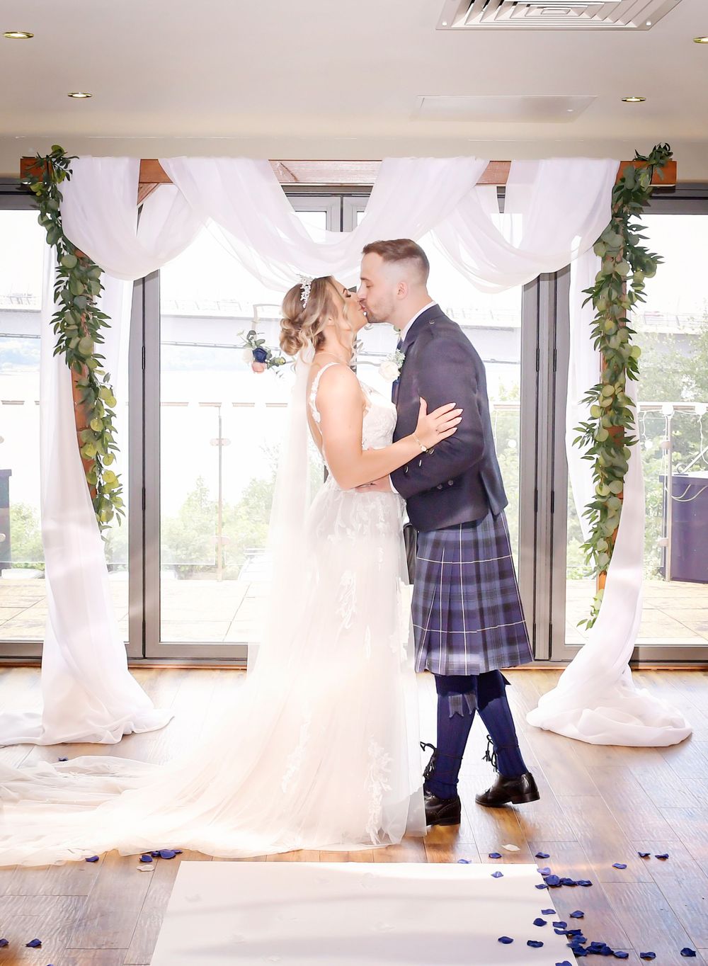 Bride and Groom share a tender kiss at their wedding ceremony in the Double Tree Hilton. Framed in front of a glass windows.