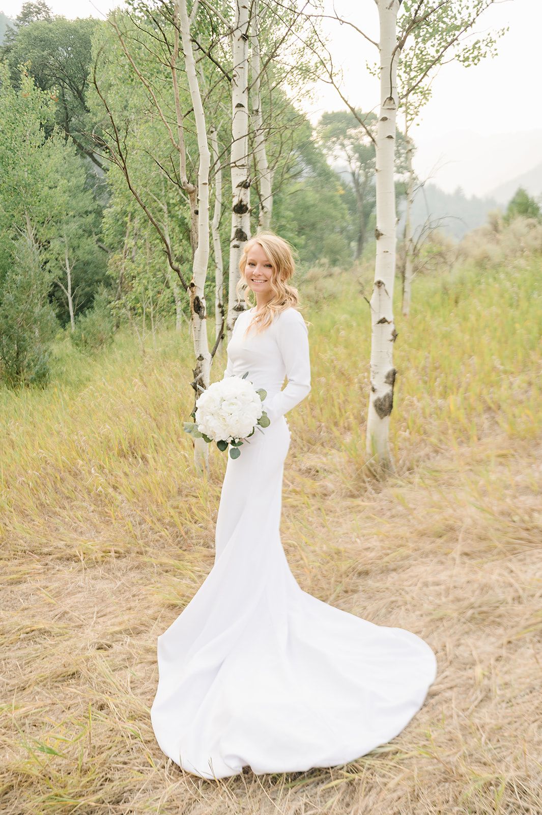 A flowing white wedding dress against a backdrop of aspen trees in a golden mountain meadow.