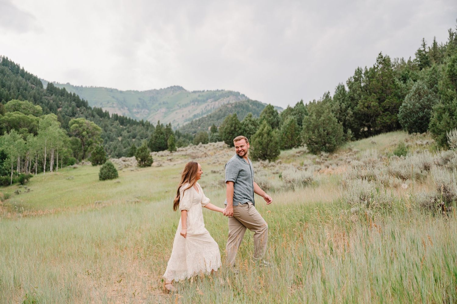 A couple dances together in a green meadow surrounded by mountain scenery.