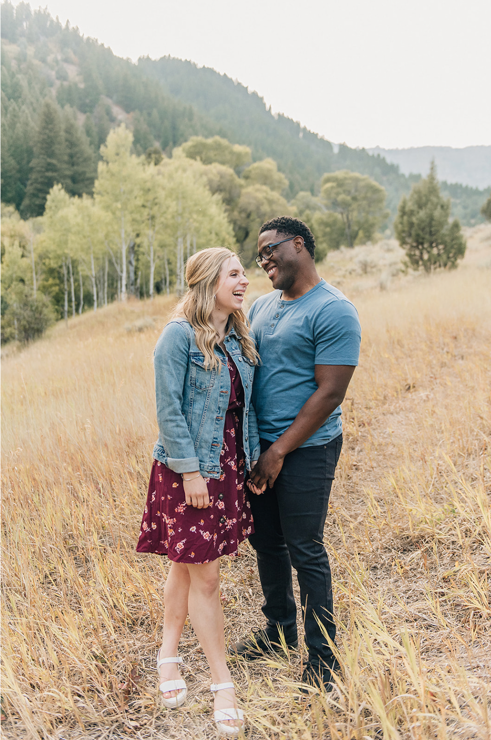 A happy couple shares a laugh together on a mountainside with autumn colors in the background.