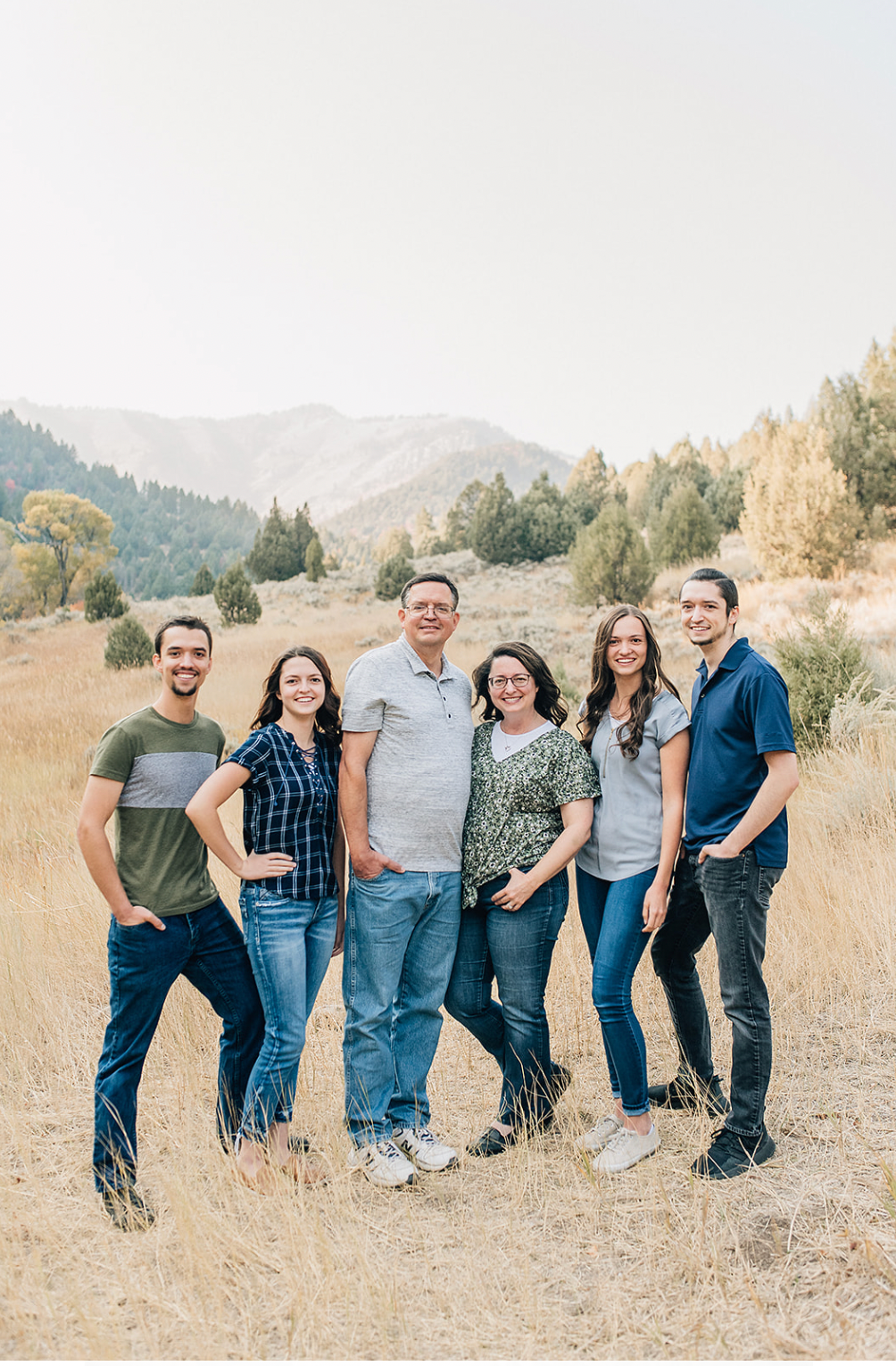 Family group poses together in casual attire against a scenic mountain backdrop with dry grass and trees.