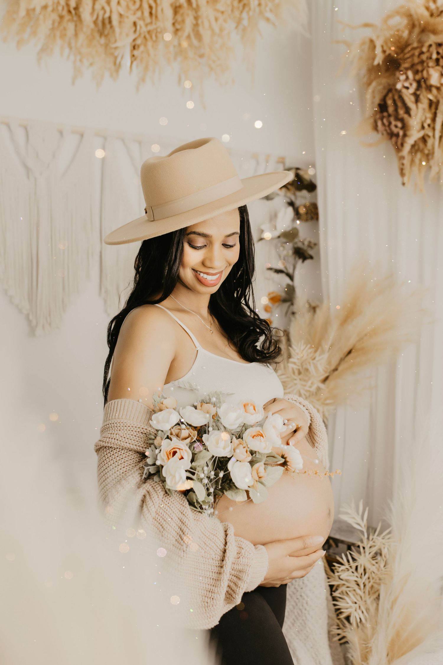 Maternity photo featuring woman in hat holding bouquet against neutral boho backdrop with pampas grass.