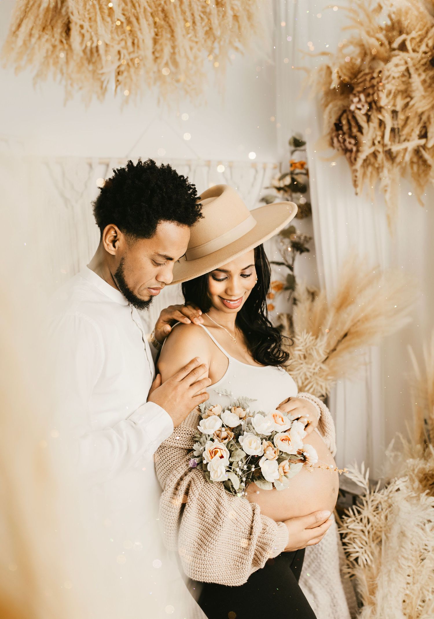 Intimate couple embraces in romantic setting with dried pampas grass decor and soft lighting.